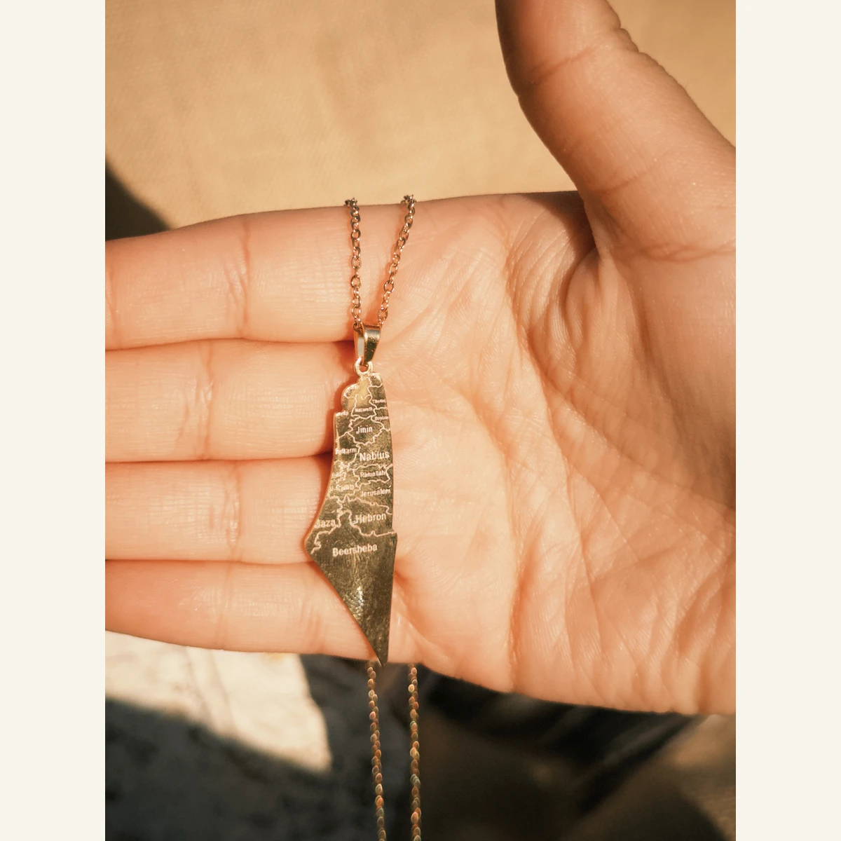 Golden Engraved Palestine Necklace held in hand to show its size