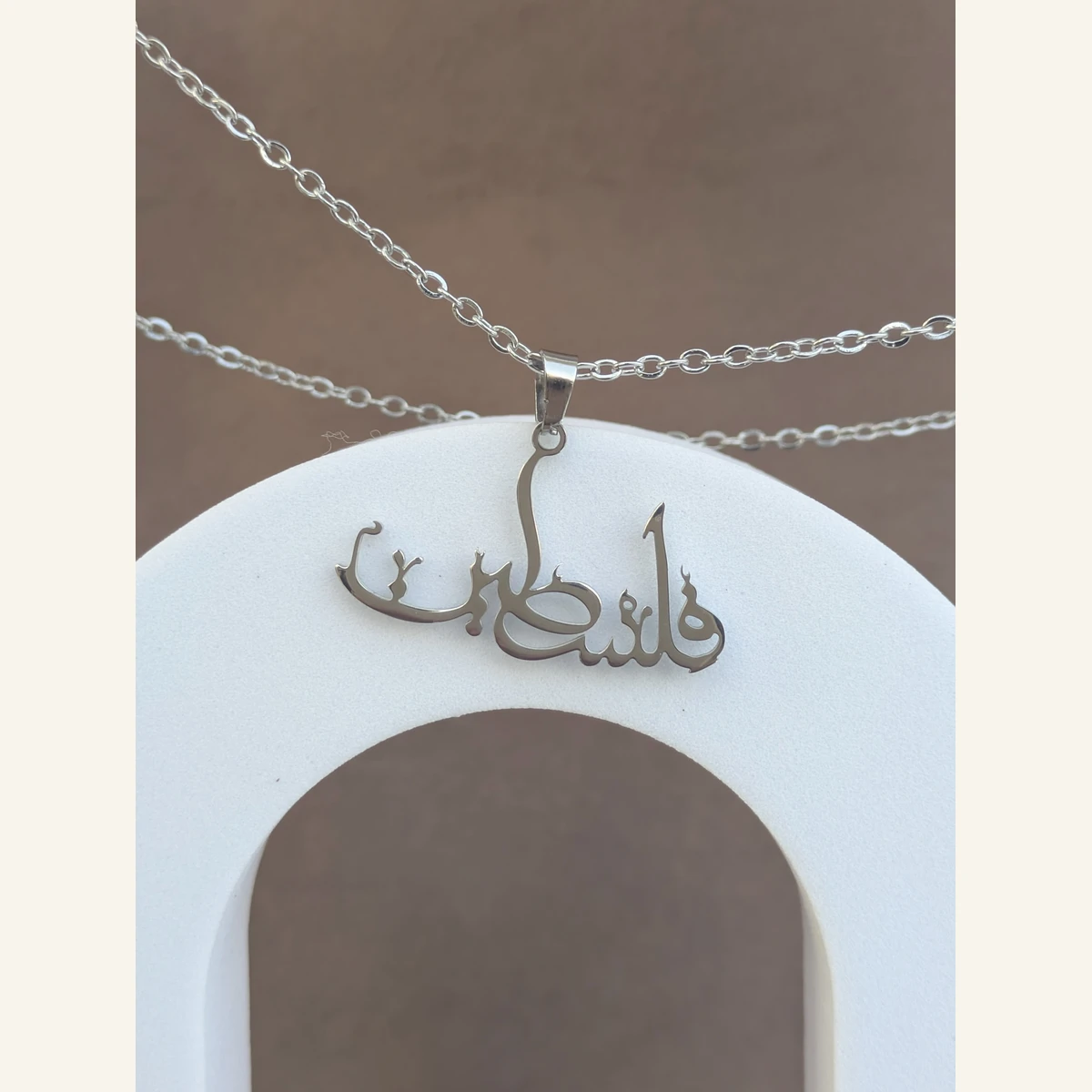 Filastin Calligraphy Necklace held in hand to show its size