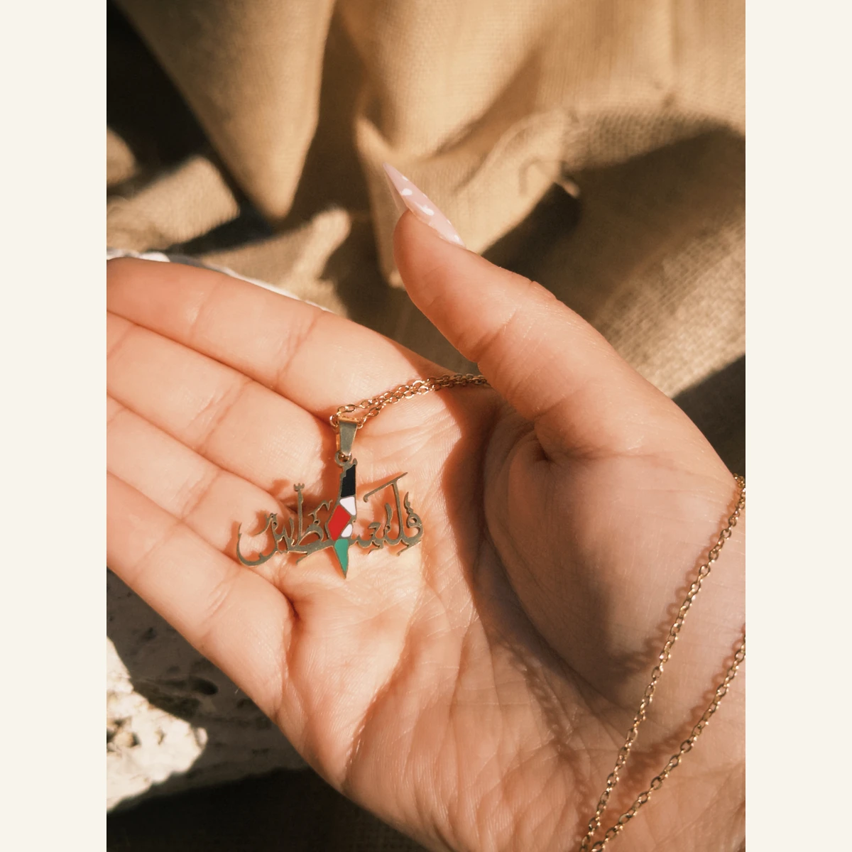 Golden Filastin Flag Necklace held in hand to show its size